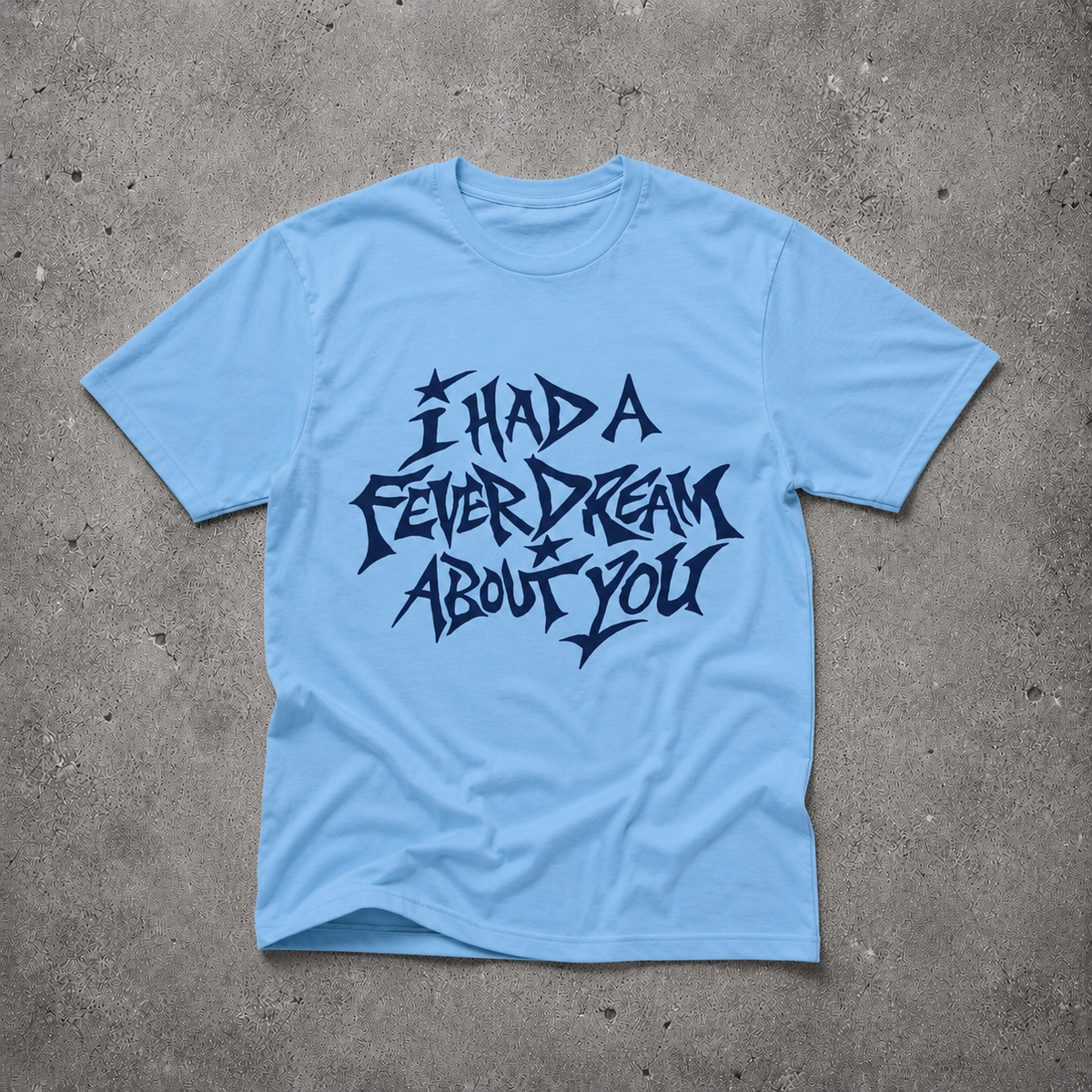 Baby blue unisex t-shirt with navy "I Had a Fever Dream About You" hand-lettered graphic print, flat lay on concrete background