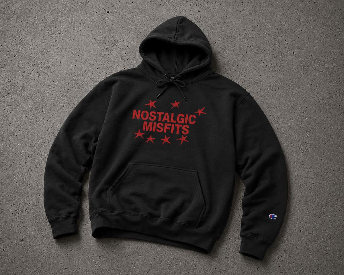 Black Nostalgic Misfits x Champion hoodie laid flat on concrete — front view showing red star logo graphic with NOSTALGIC MISFITS text and Champion C logo embroidered on the left sleeve