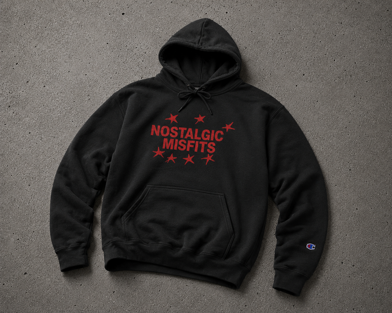 Black Nostalgic Misfits x Champion hoodie laid flat on concrete — front view showing red star logo graphic with NOSTALGIC MISFITS text and Champion C logo embroidered on the left sleeve