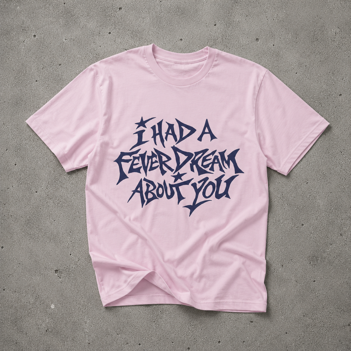 Pink unisex t-shirt with navy "I Had a Fever Dream About You" hand-lettered graphic print, flat lay on concrete background