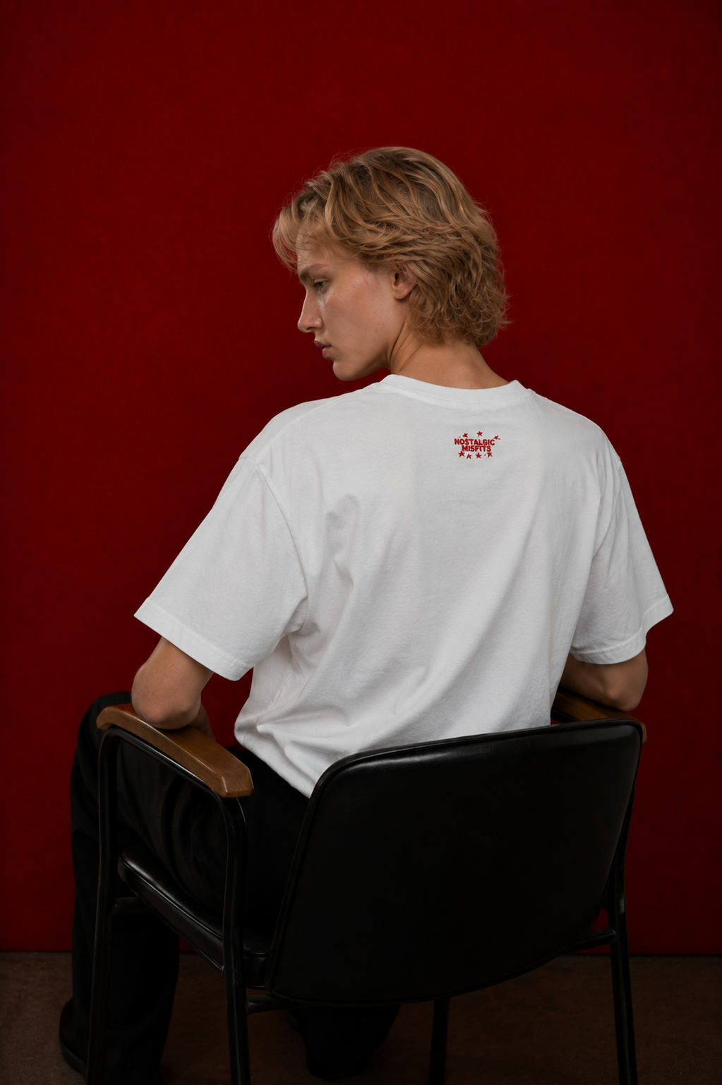 Model wearing Saint Maddy tee, back view with red NM logo, dark red background — Nostalgic Misfits EUPHORIC drop 003
