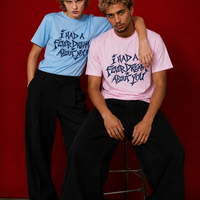 Two models wearing "I Had a Fever Dream About You" t-shirts against a deep red background — one in baby blue, one in pink, with navy graphic print