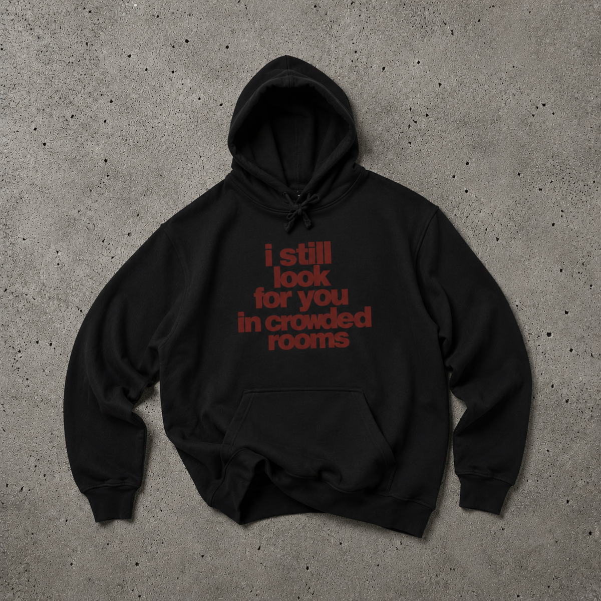 Black Nostalgic Misfits hoodie laid flat on concrete — front view showing dark red bold typographic print reading "i still look for you in crowded rooms" in stacked lowercase letters