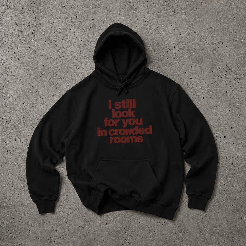 Black Nostalgic Misfits hoodie laid flat on concrete — front view showing dark red bold typographic print reading "i still look for you in crowded rooms" in stacked lowercase letters